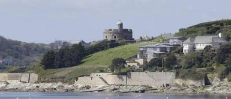 A coastal town with a prominent lighthouse on a hill, houses along the shoreline, and a calm sea with buoys.