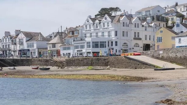 A coastal hotel with multiple stories, a prominent sign, and a beach in the foreground.