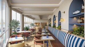 A restaurant with a long bench seating area, tables, chairs, and a view of the water.