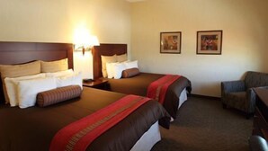 Habitación de hotel con dos camas, una mesita de noche, una lámpara, una silla y dos cuadros en la pared.