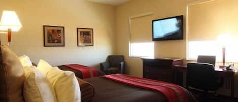 A hotel room with a bed, two chairs, a desk, a television, and two framed pictures on the wall.