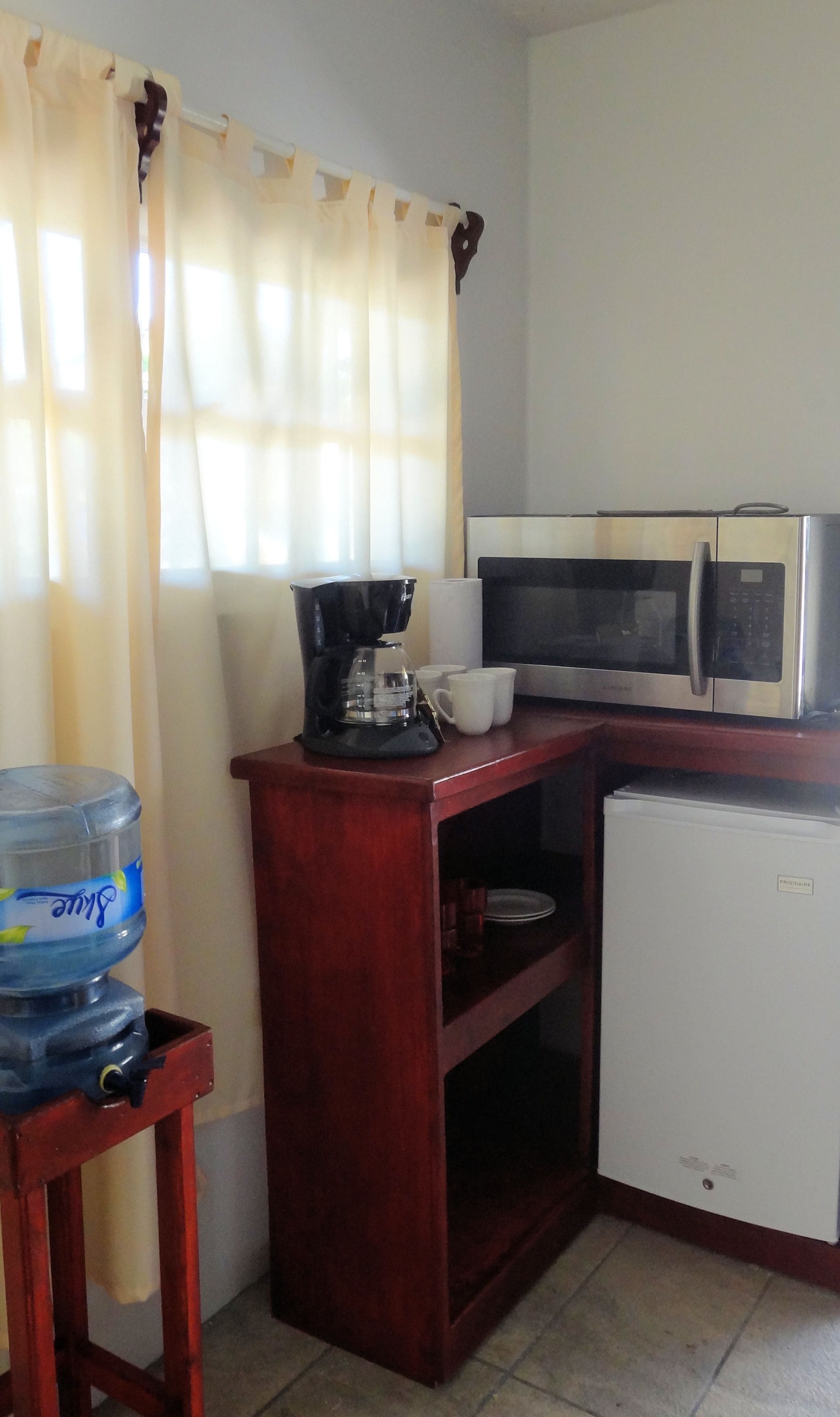 Una kitchenette compacta con microondas, cafetera y dispensador de agua.