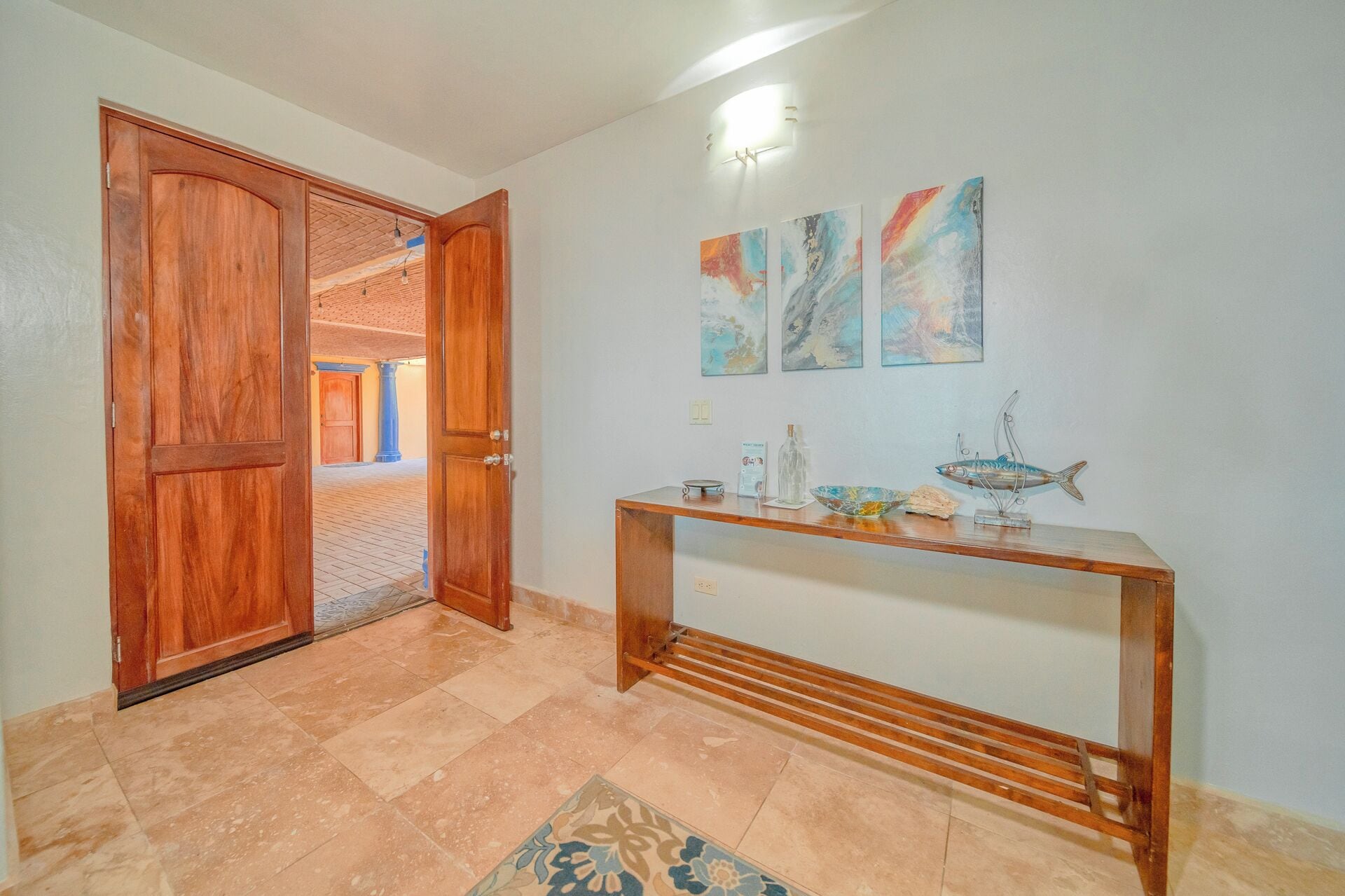 A hallway with a wooden door, a tiled floor, a console table with decorative items, and abstract wall art.