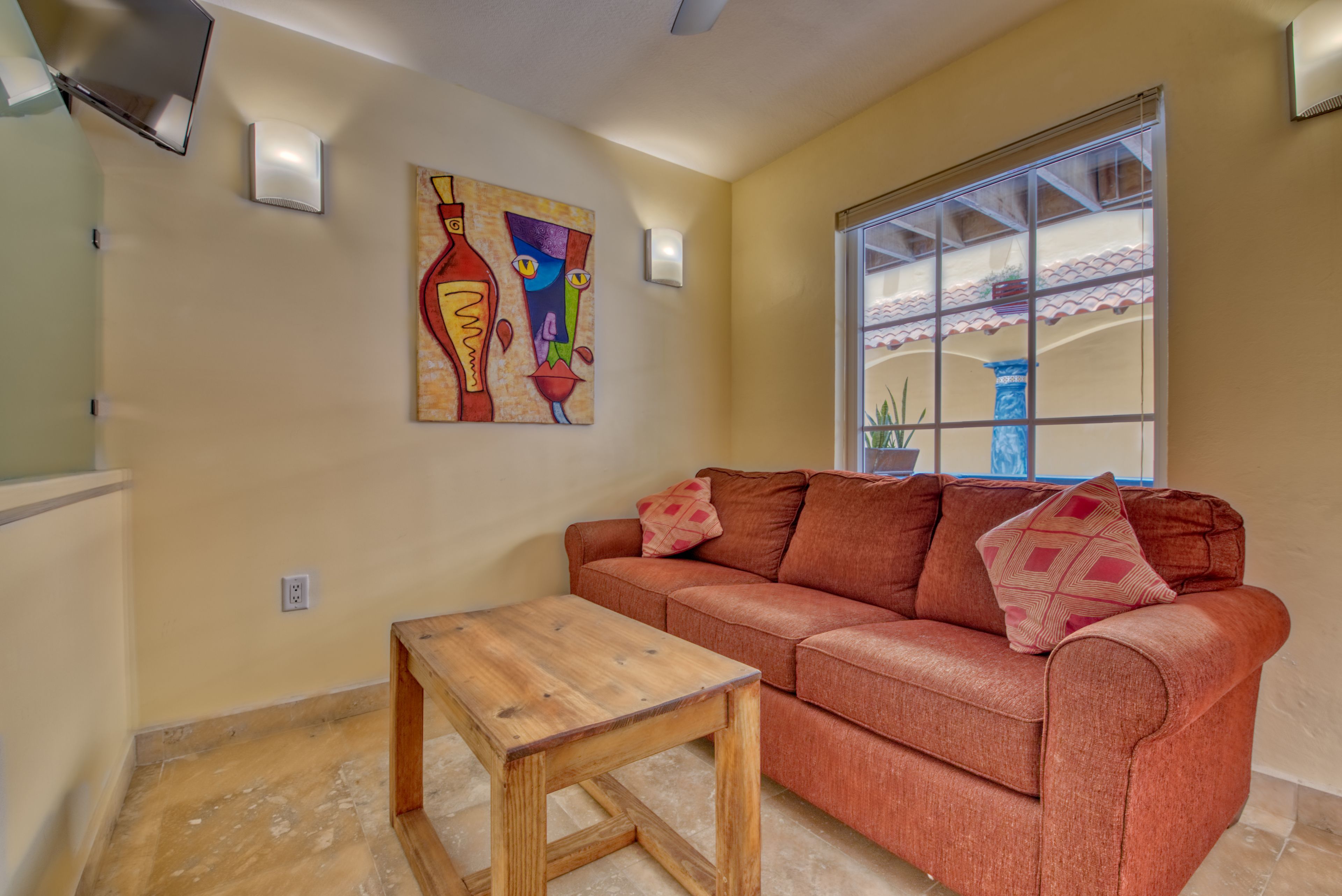 A living room with a red sofa, a wooden coffee table, and a colorful abstract painting on the wall.