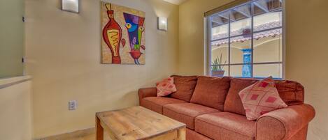 A living room with a red sofa, a wooden coffee table, and a colorful abstract painting on the wall.