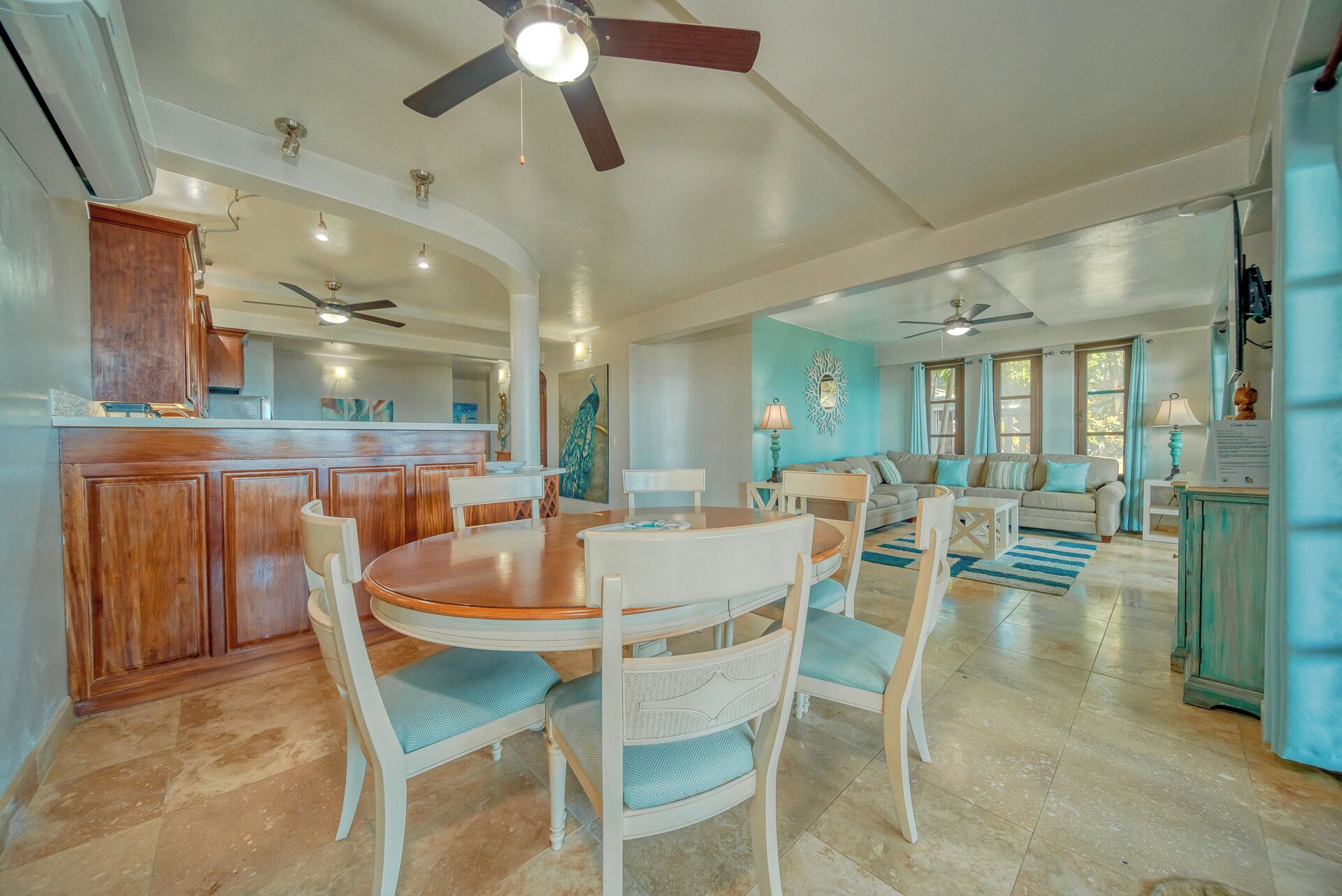 A spacious living area with a dining table and chairs, a kitchen with wooden cabinets, and a ceiling fan.