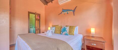A bedroom with a bed, pillows, a nightstand, a wall-mounted air conditioner, and a door.
