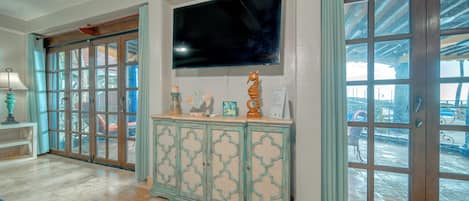 A spacious room with a large TV mounted on the wall, a wooden cabinet with decorative items, and a view through a glass door.
