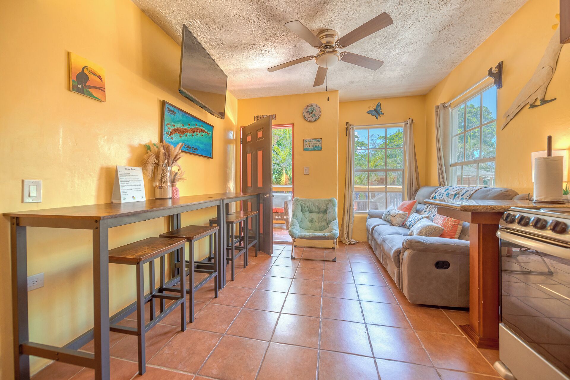 A kitchen with a stove, a dining table with chairs, a ceiling fan, and a window with curtains.