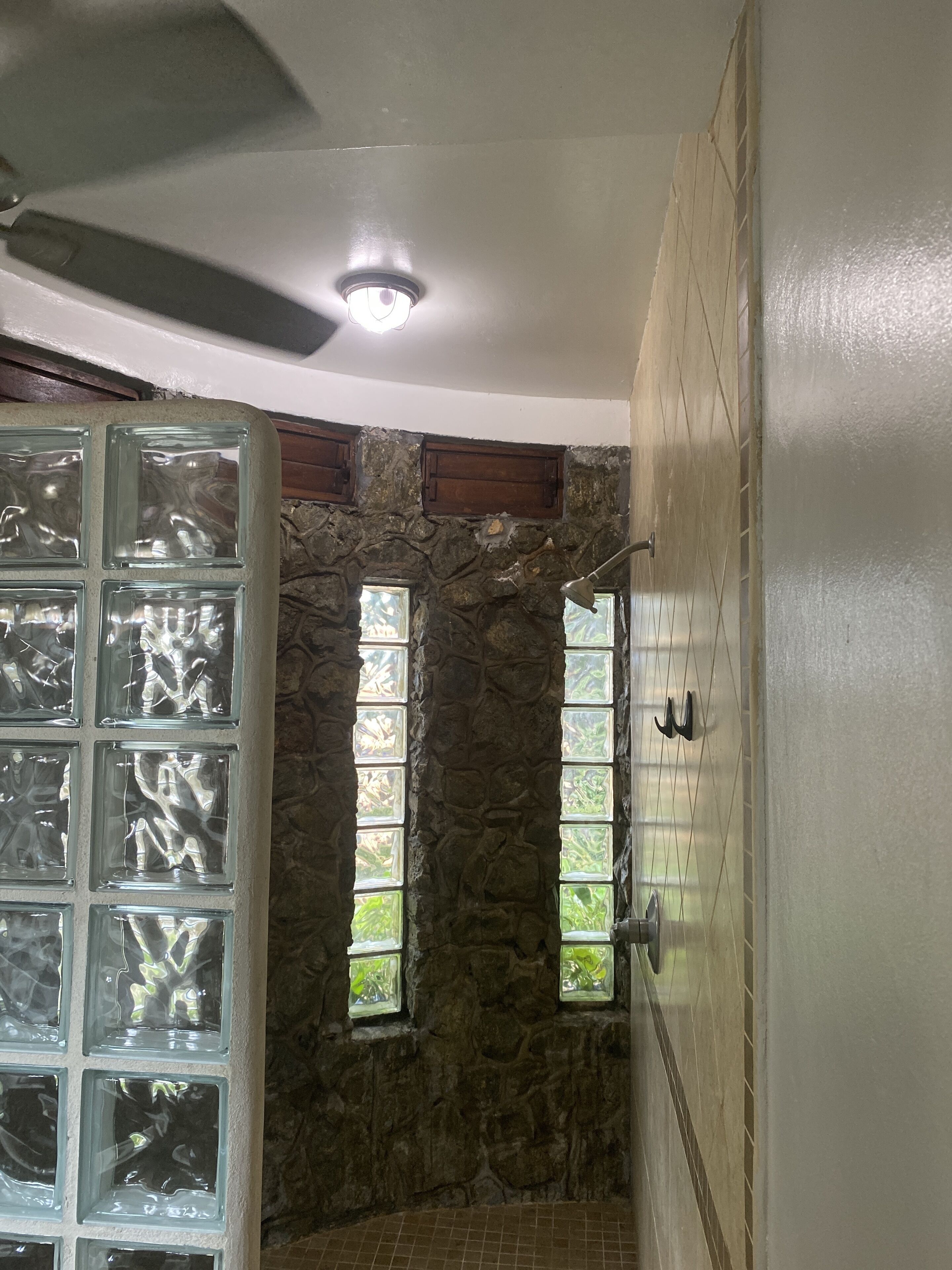 A bathroom with a stone wall, a glass shower enclosure, and a ceiling fan.