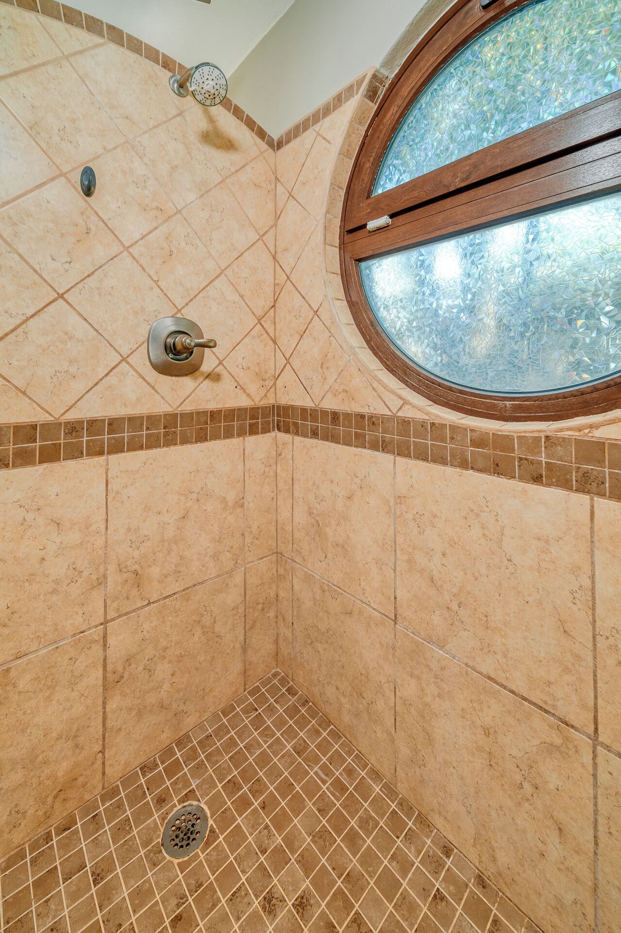 Un bagno con doccia, pareti piastrellate, una finestra e uno scarico.