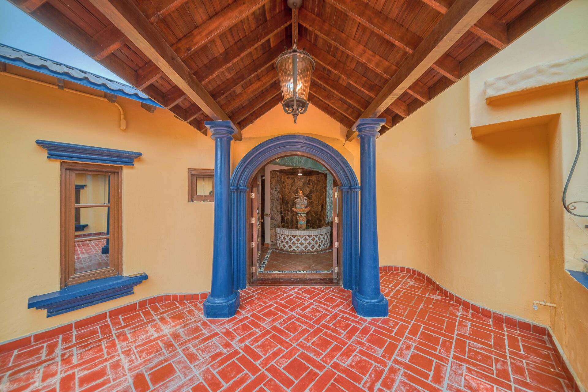 A hallway with red-tiled flooring, blue columns, and a wooden ceiling.