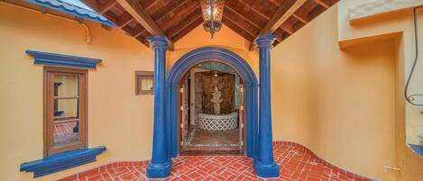 A hallway with red-tiled flooring, blue columns, and a wooden ceiling.