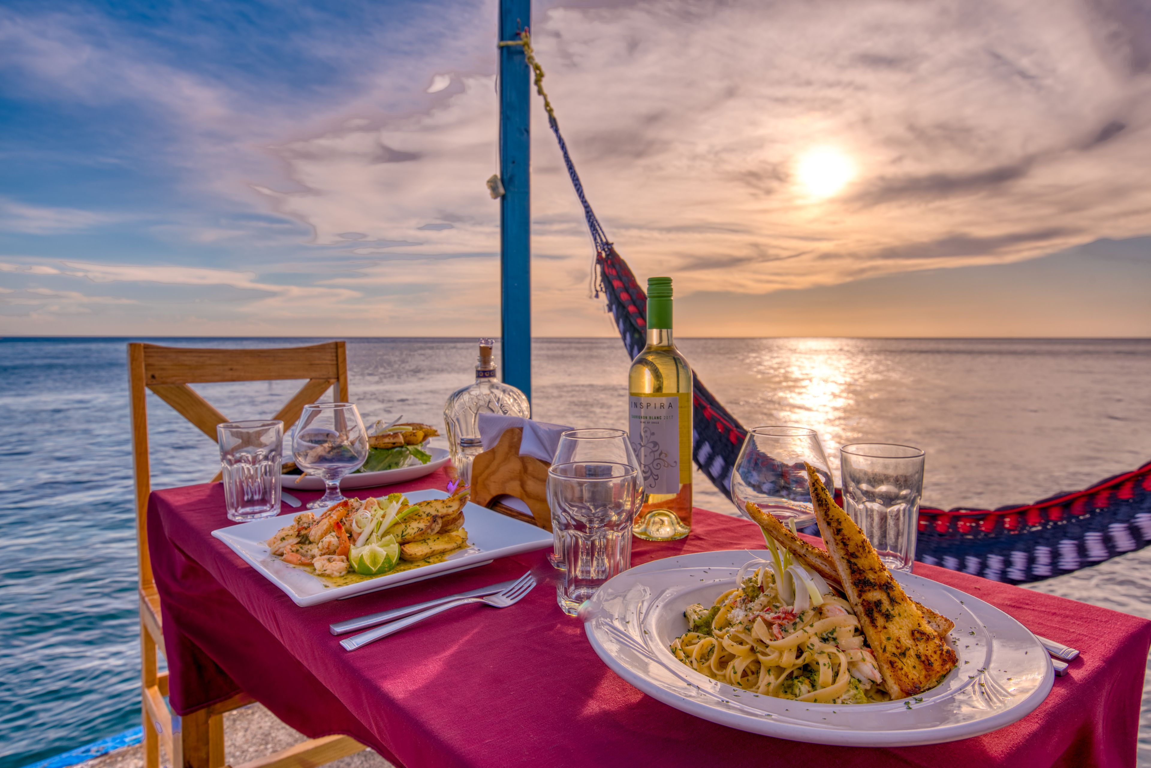 A table set for two with a sunset view, a bottle of wine, and plates of food.