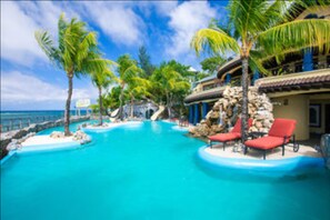 A resort pool with palm trees and a view of the ocean. - Caribe Tesoro (Roatan)