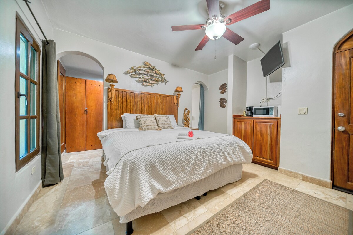 Une chambre à coucher avec un lit, une armoire en bois, un ventilateur de plafond et un téléviseur fixé au mur.