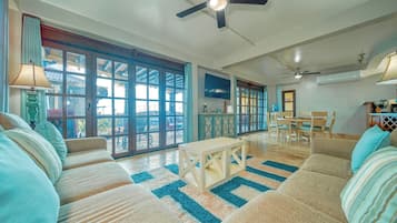 A spacious living room with a large window, a ceiling fan, and a dining area with wooden furniture.