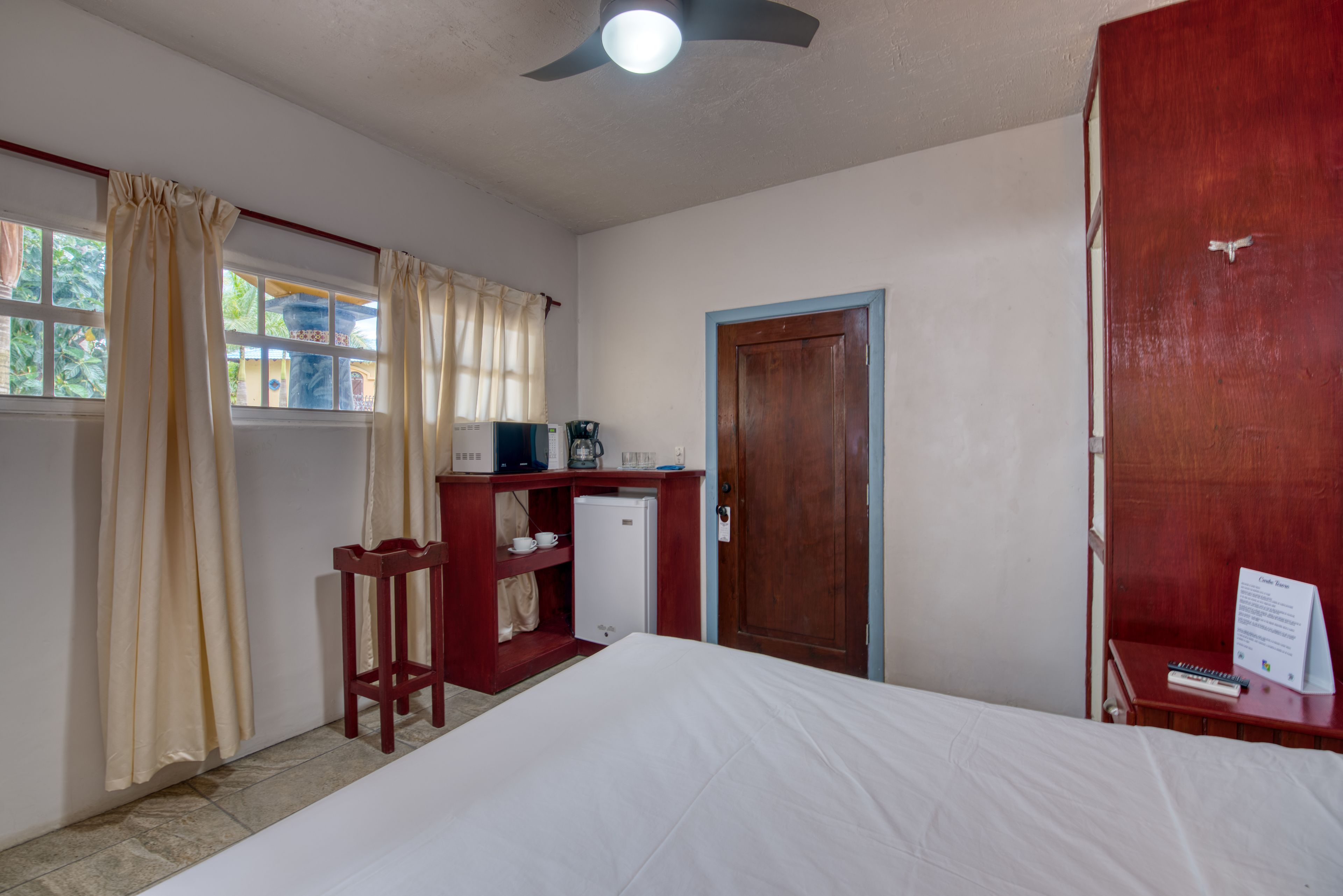 A hotel room with a bed, a desk with a computer, a small refrigerator, and a wooden wardrobe.