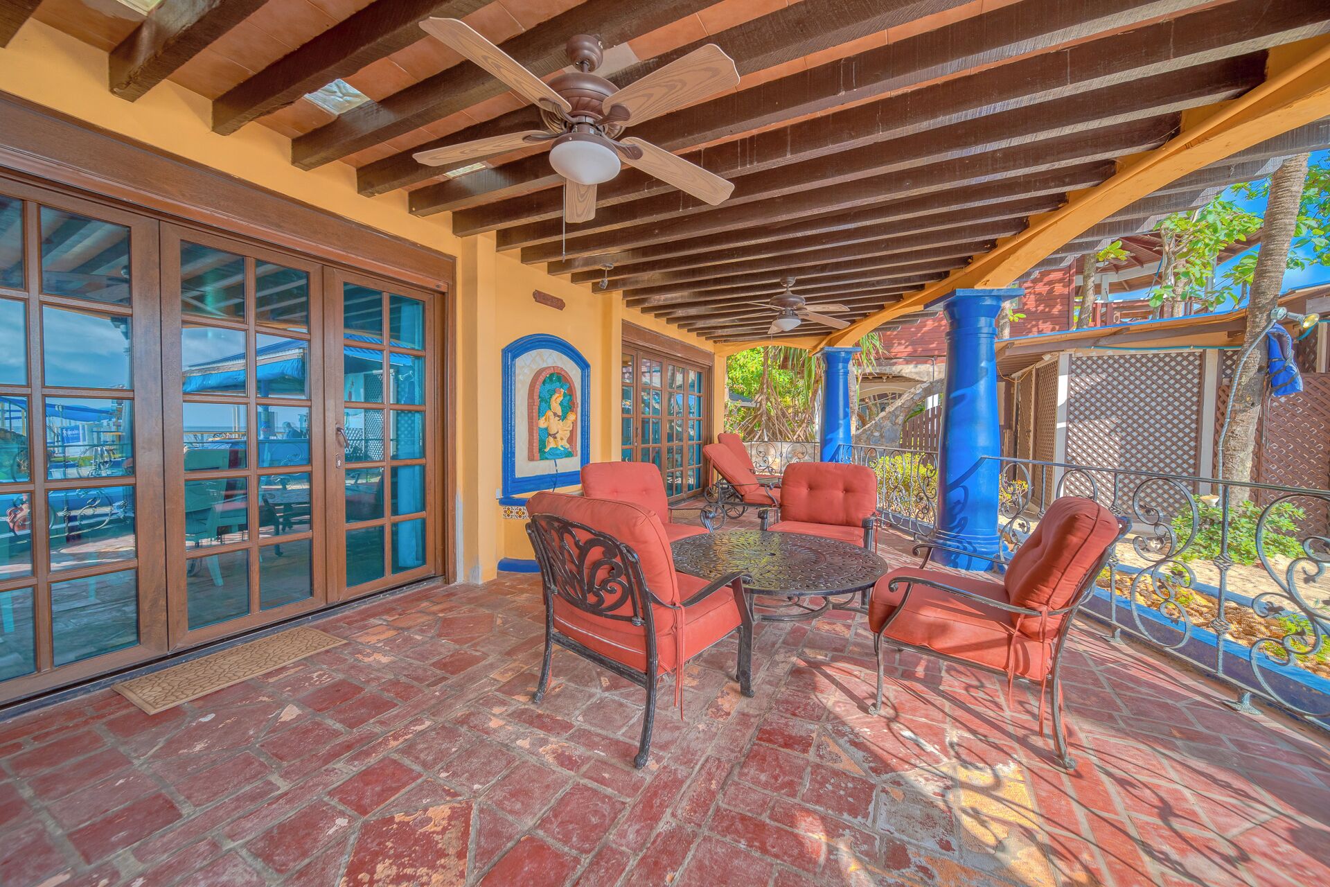 A covered patio with red cushioned chairs, a round table, and a ceiling fan.
