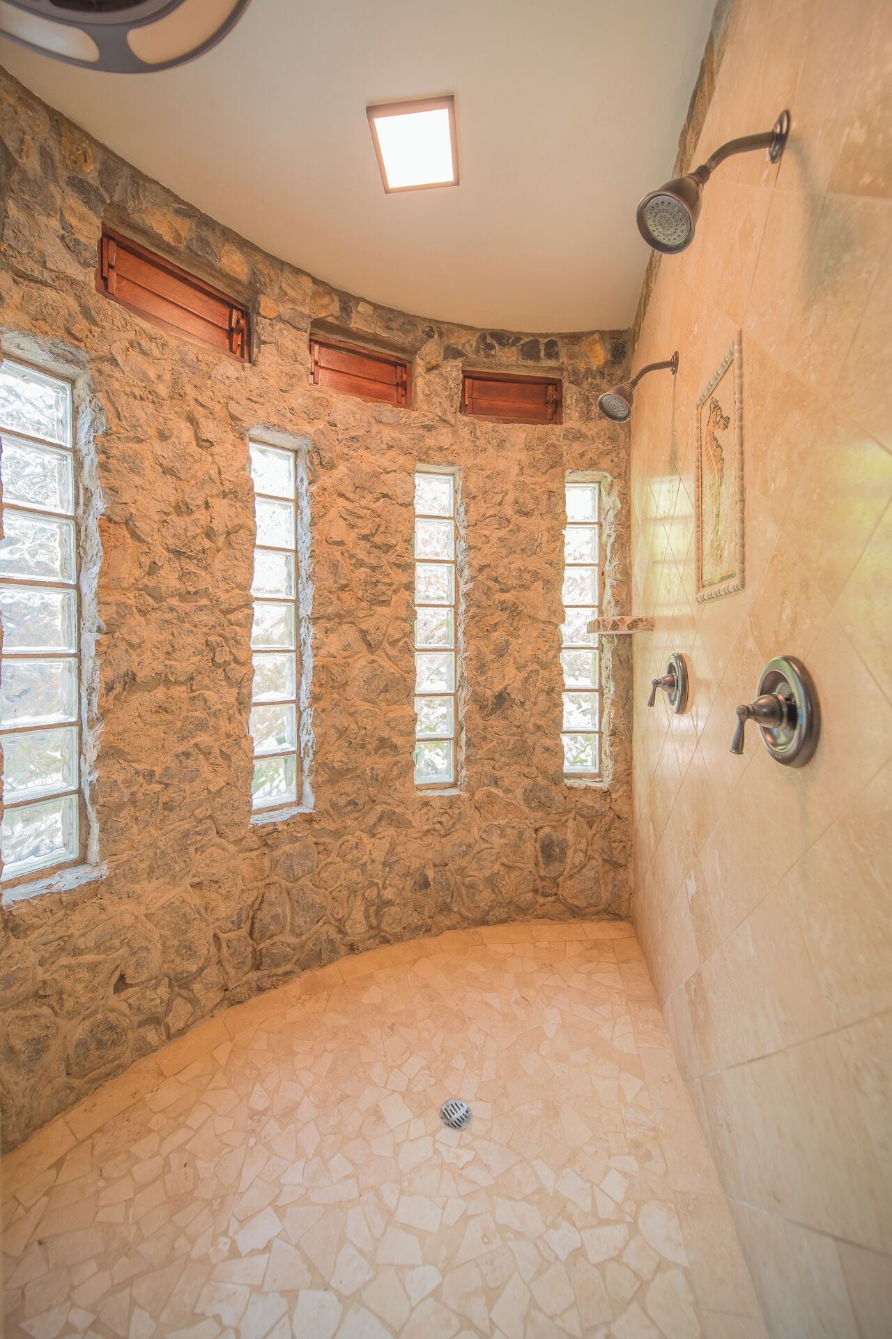 A stone-walled bathroom with a shower, a tiled floor, and three windows.