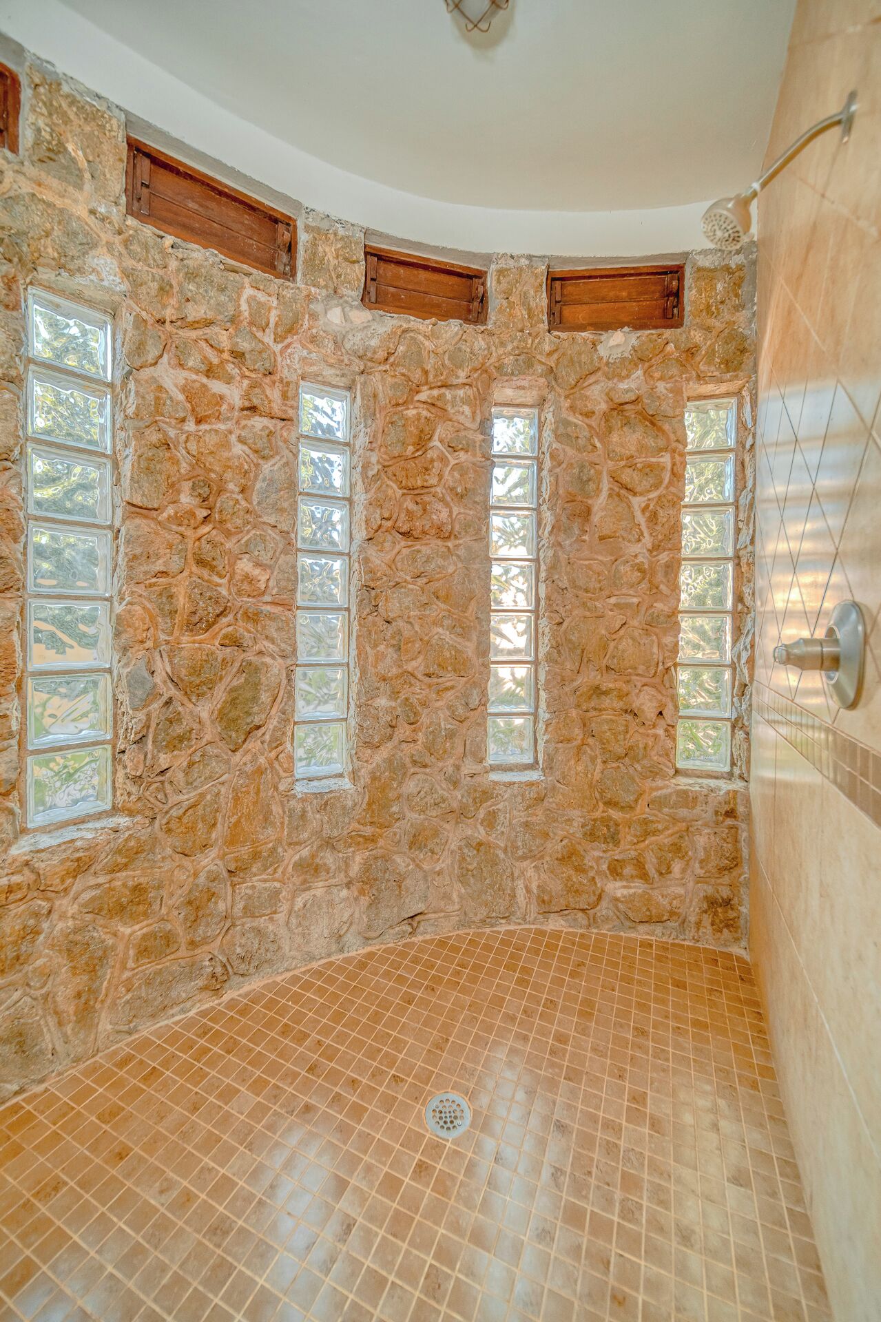 Une salle de bain aux murs en pierre, dotée d’un sol carrelé, d’une zone douche et d’une fenêtre.