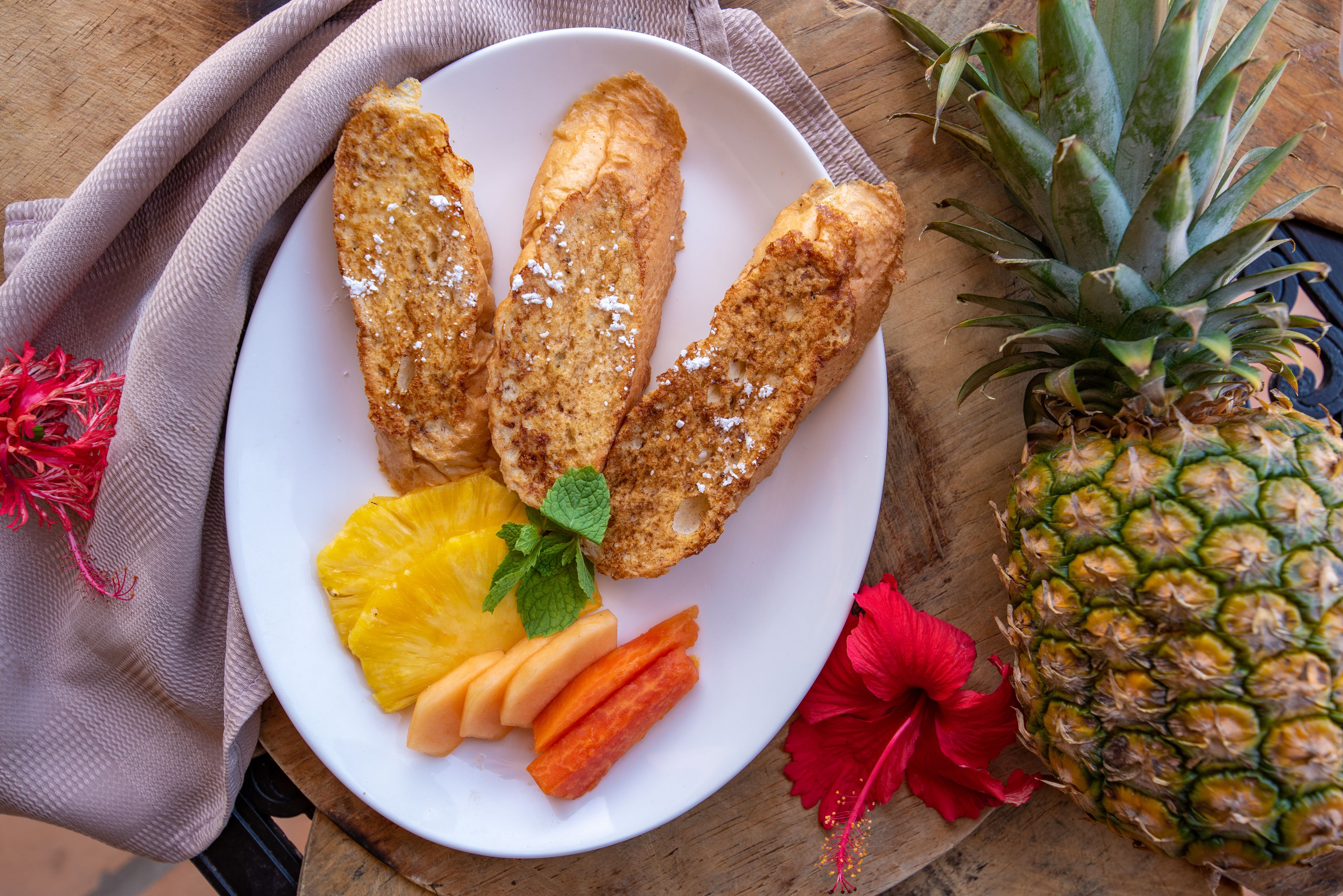 A plate with three pieces of bread, a slice of pineapple, and some carrot sticks on a wooden table.