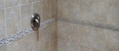 A shower area with tiled walls and floor, a showerhead, and a drain.