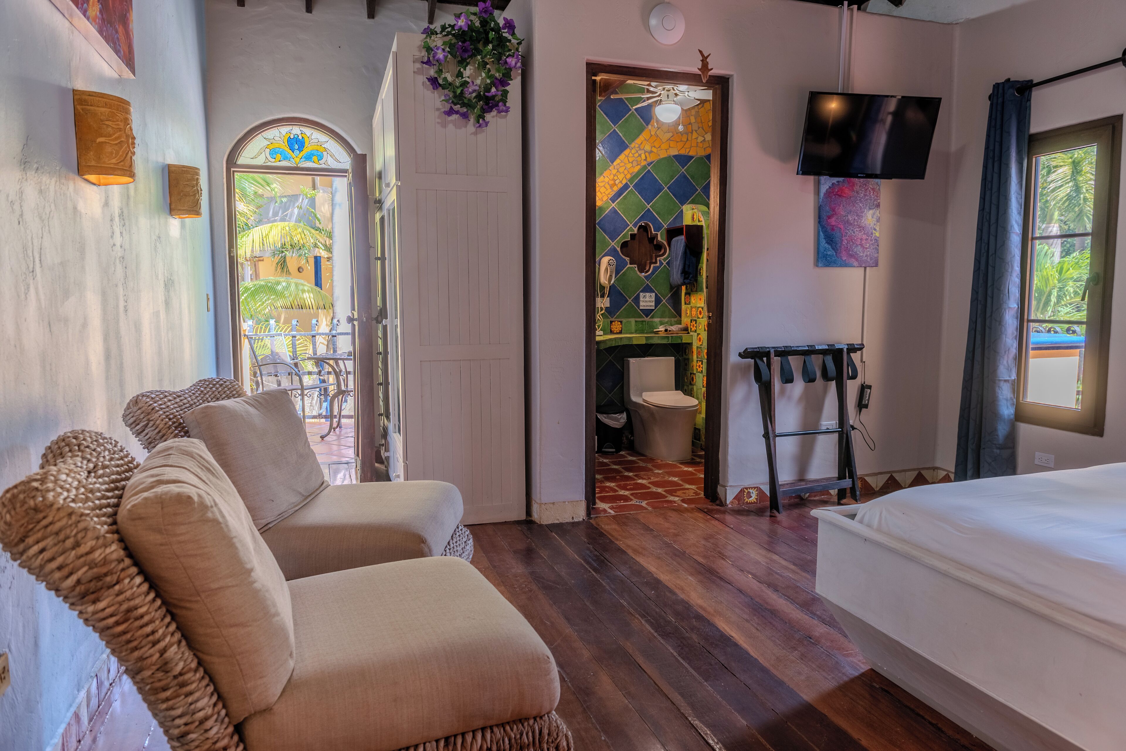 Quarto com uma cama, duas poltronas, televisão e um banheiro visível por uma porta aberta.