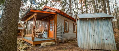 A cabin with a porch, a small shed, and a wooden deck.