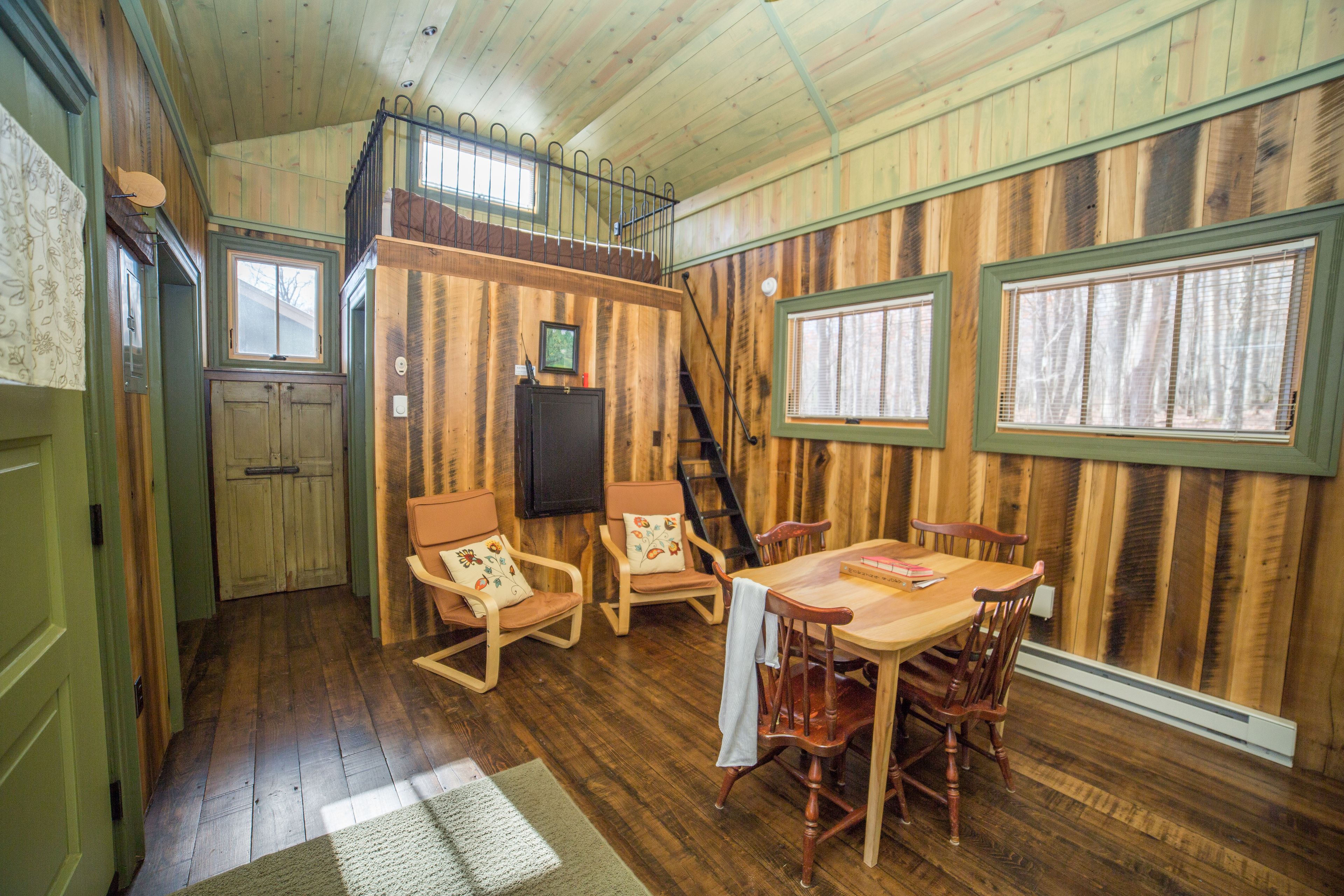 A cozy cabin interior with a dining area, wooden walls, and a loft bedroom.