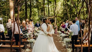 A wedding ceremony in a forested area with wooden benches and flower arrangements. - Blue Moon Rising (McHenry)