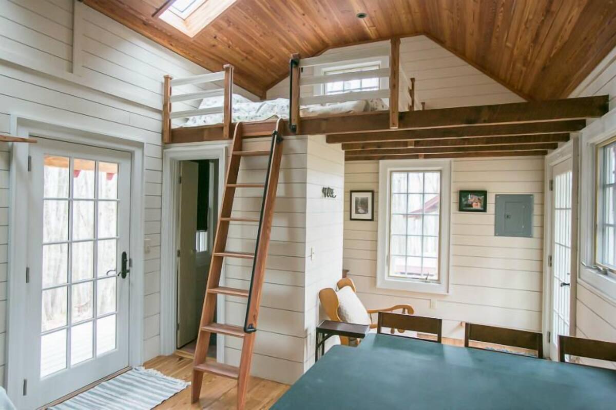 A loft-style room with a wooden ladder, a dining table, and a bunk bed.