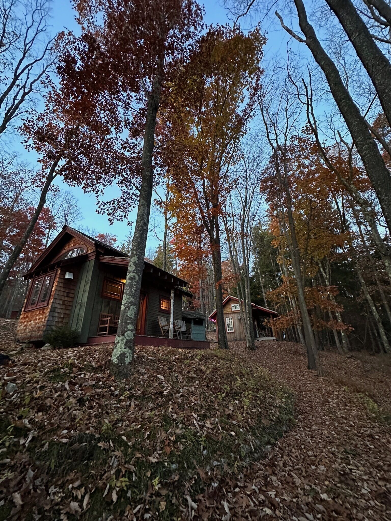Eine Hütte mit Veranda und Stühlen, umgeben von Bäumen mit Herbstlaub.