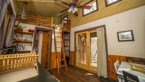 A rustic cabin interior with a loft bed, wooden furniture, a ceiling fan, and a dining area. - Blue Moon Rising (McHenry)