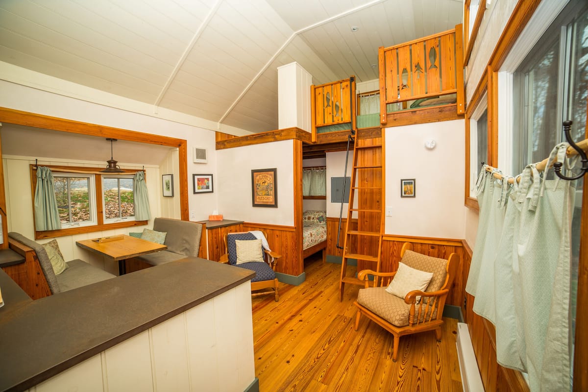 A cozy cabin interior with a loft bed, a dining area, and a seating space.