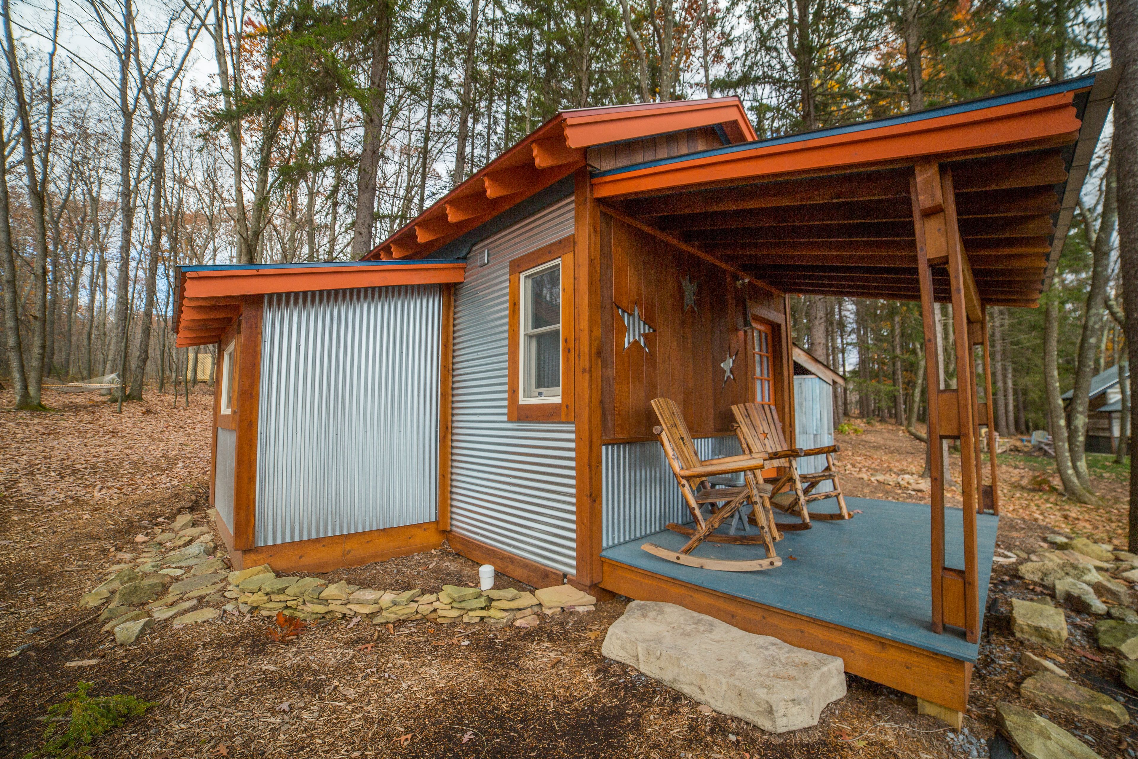Une cabane rustique dotée d’une véranda, de chaises berçantes en bois et d’un sentier pavé de pierres.