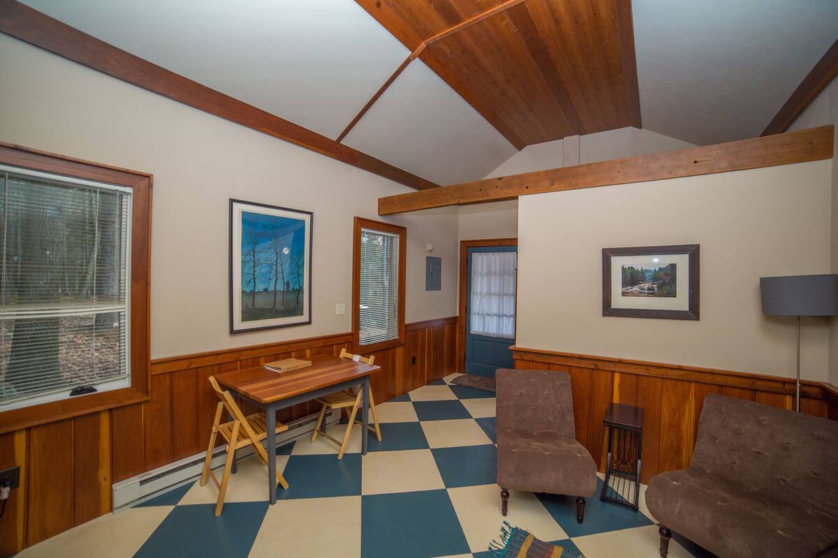 A room with a wooden dining table, two armchairs, a checkered floor, and wooden walls.