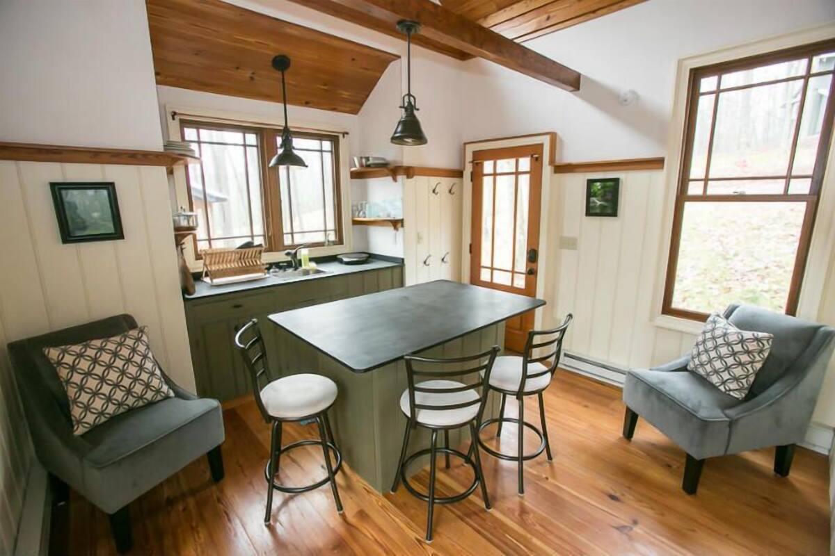 A kitchen with a central island, bar stools, and a dining area with a sofa and chairs.