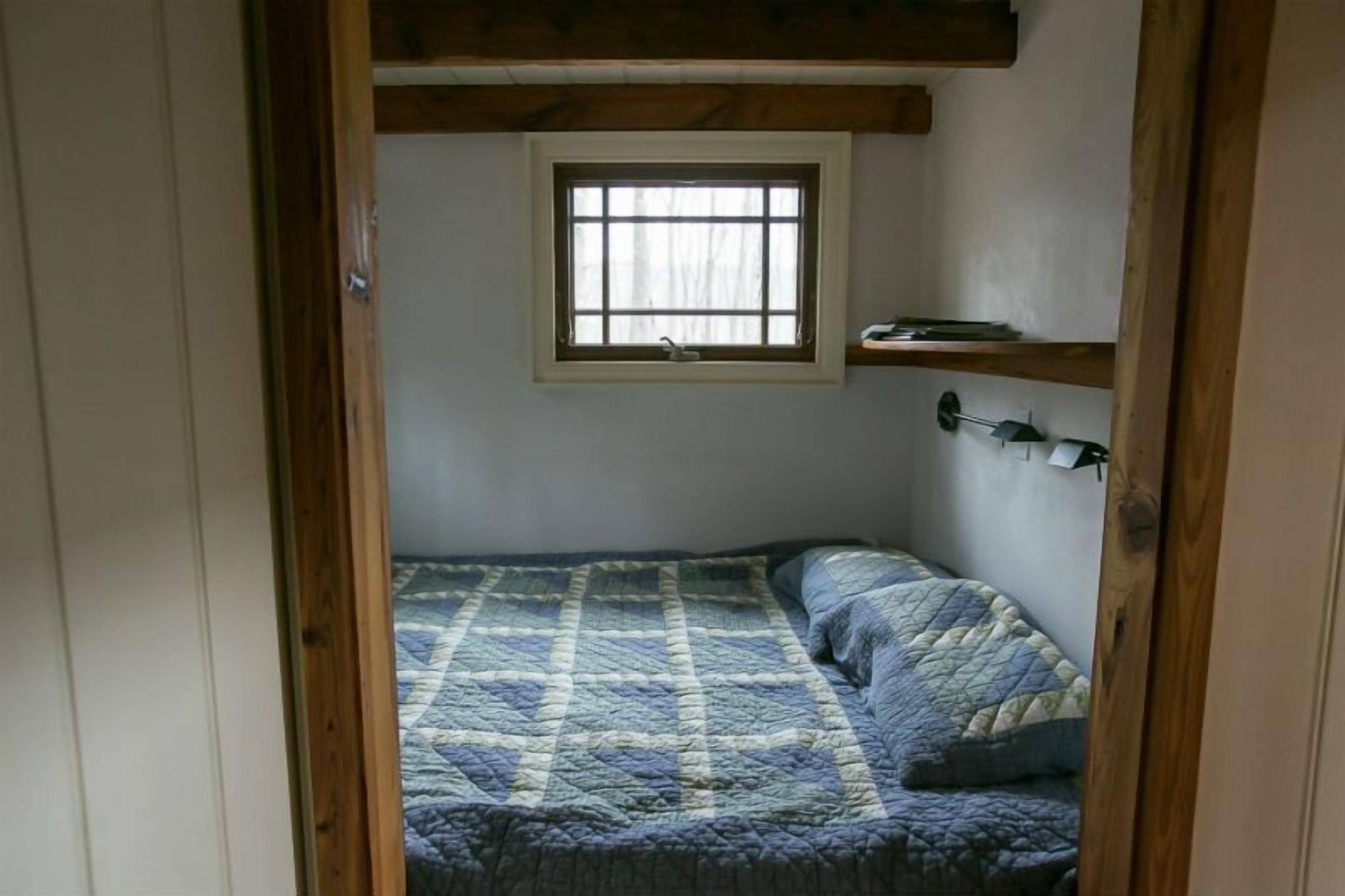 A small, cozy bedroom with a single bed, a window, and a shelf above the bed.