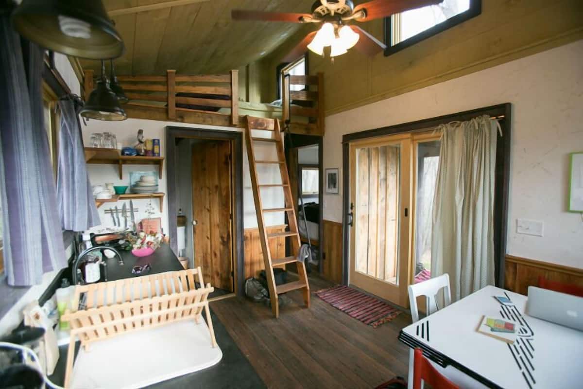 A compact, rustic kitchen with wooden accents, a dining area with a table and chairs, and a loft bedroom with a ladder.