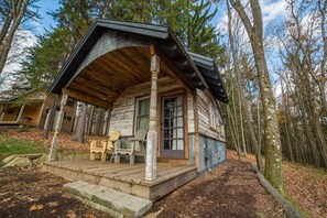 A rustic cabin with a wooden porch, a door, and a window.
