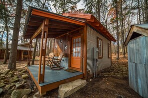 A rustic cabin with a porch, a rocking chair, and a small deck.