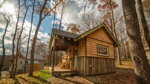 A wooden cabin with a porch and a small shed, surrounded by trees and a clear sky. - Blue Moon Rising (McHenry)