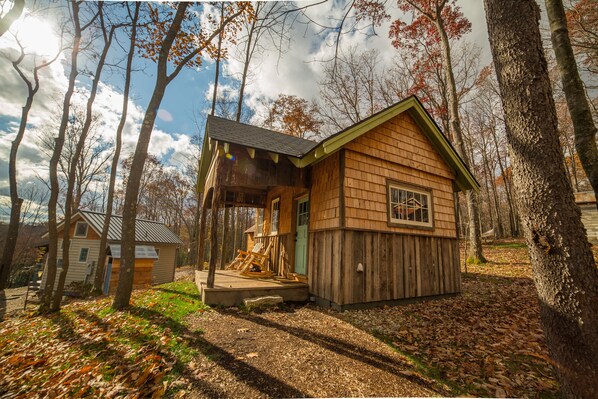 A wooden cabin with a porch and a small shed, surrounded by trees and a clear sky.