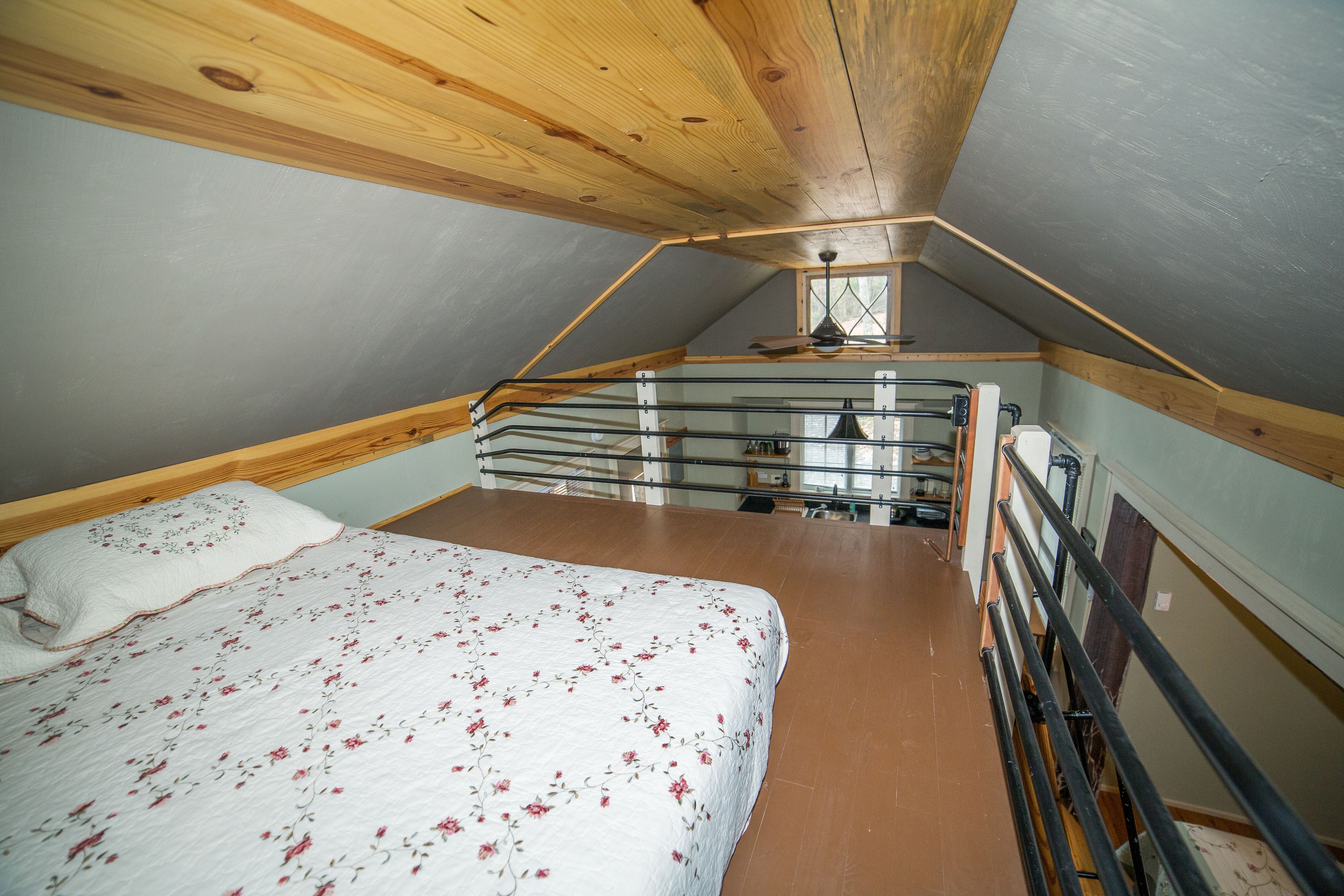A bedroom with a sloped ceiling, a bed with a floral bedspread, and a window with a view of the outside.