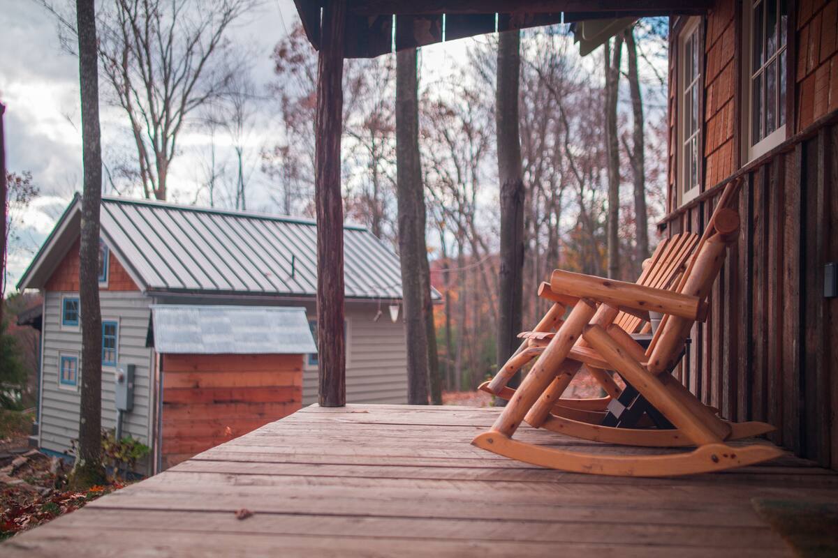 A wooden rocking chair on a porch with a view of a house and trees.