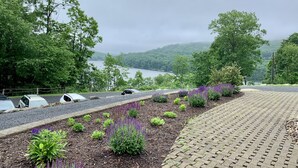 A paved walkway with a landscaped garden and a view of a lake and hills. - Blue Moon Rising (McHenry)