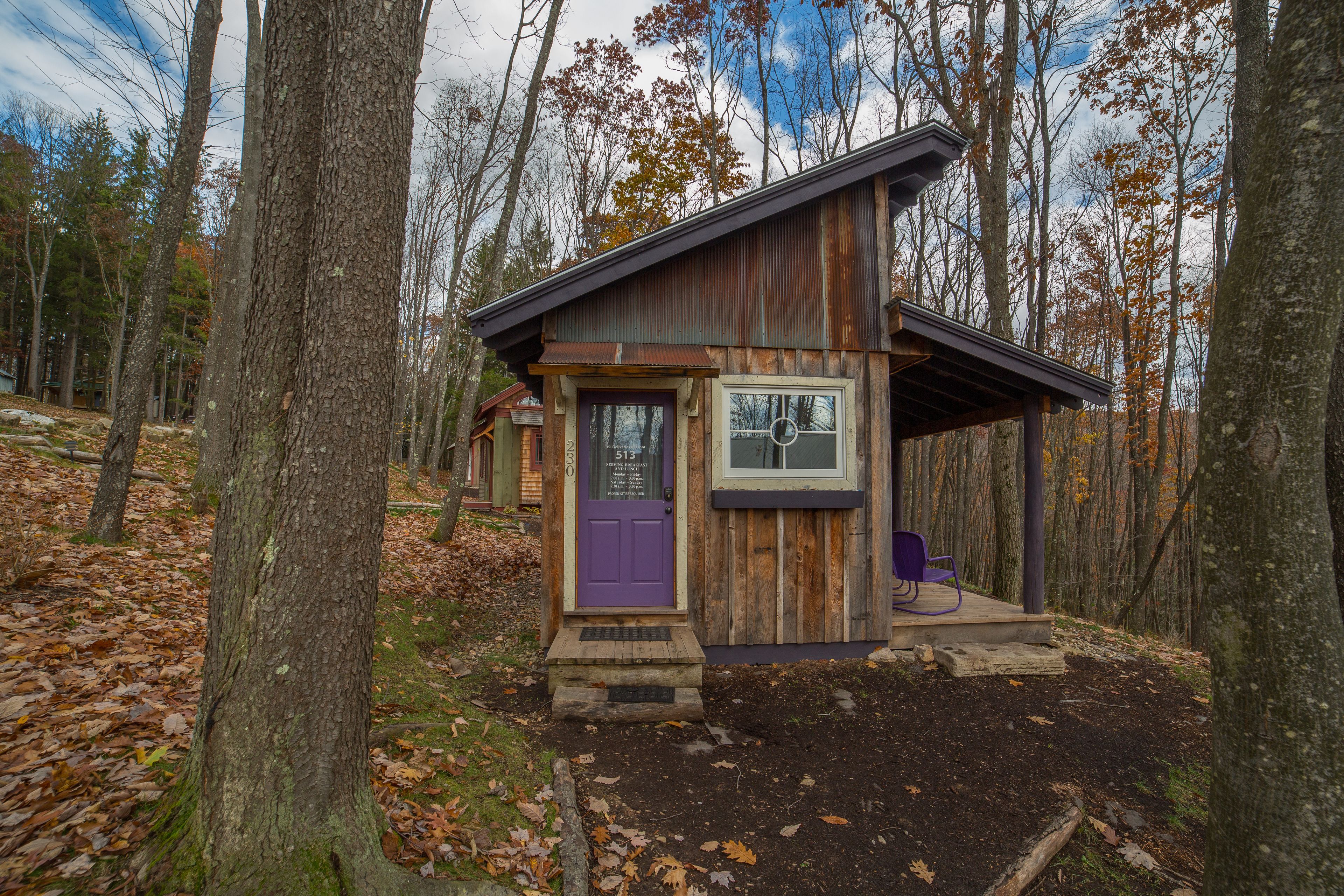 A rustic cabin with a purple door, a small porch, and a window.