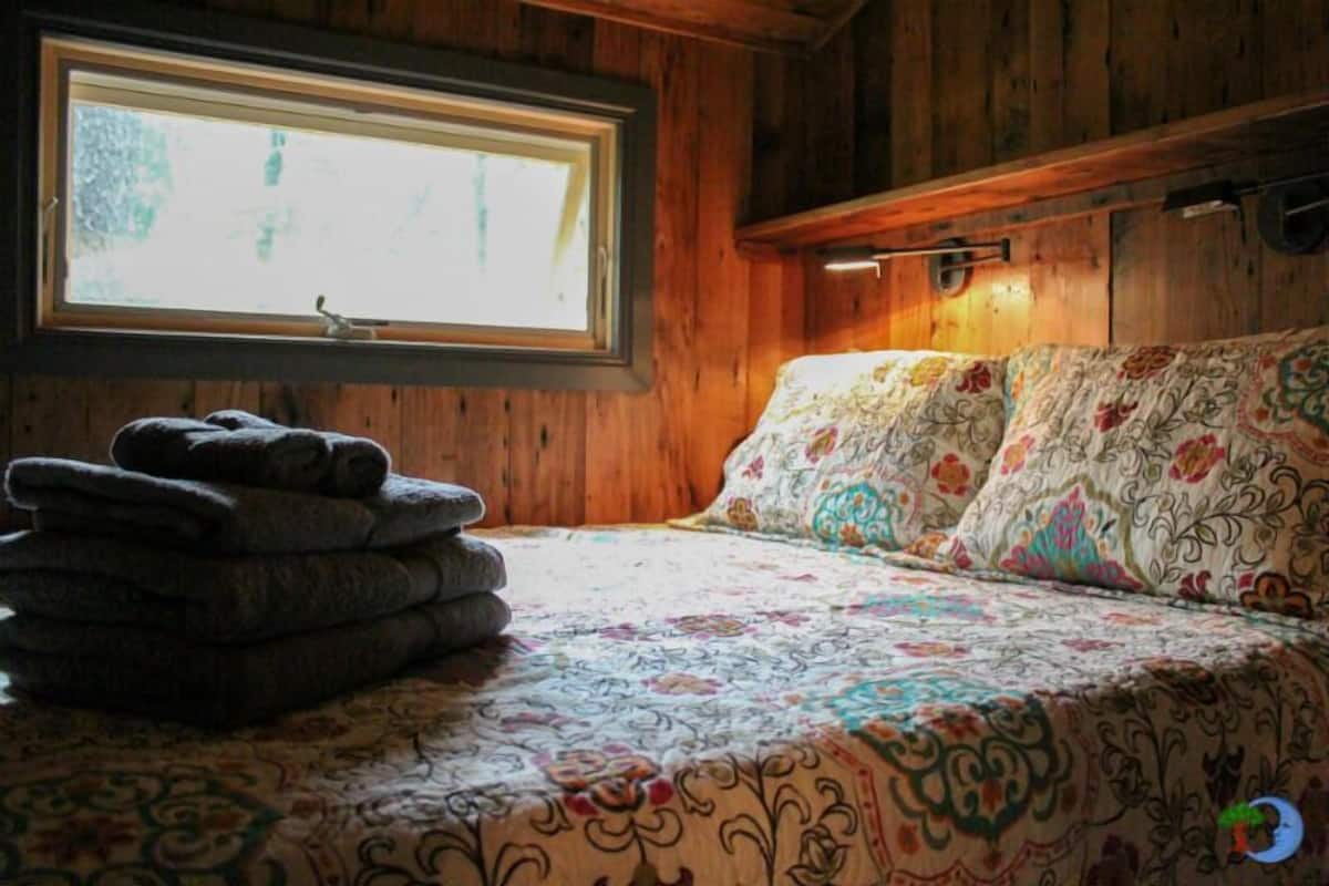 A wooden cabin room with a bed, a window, and a stack of folded towels.