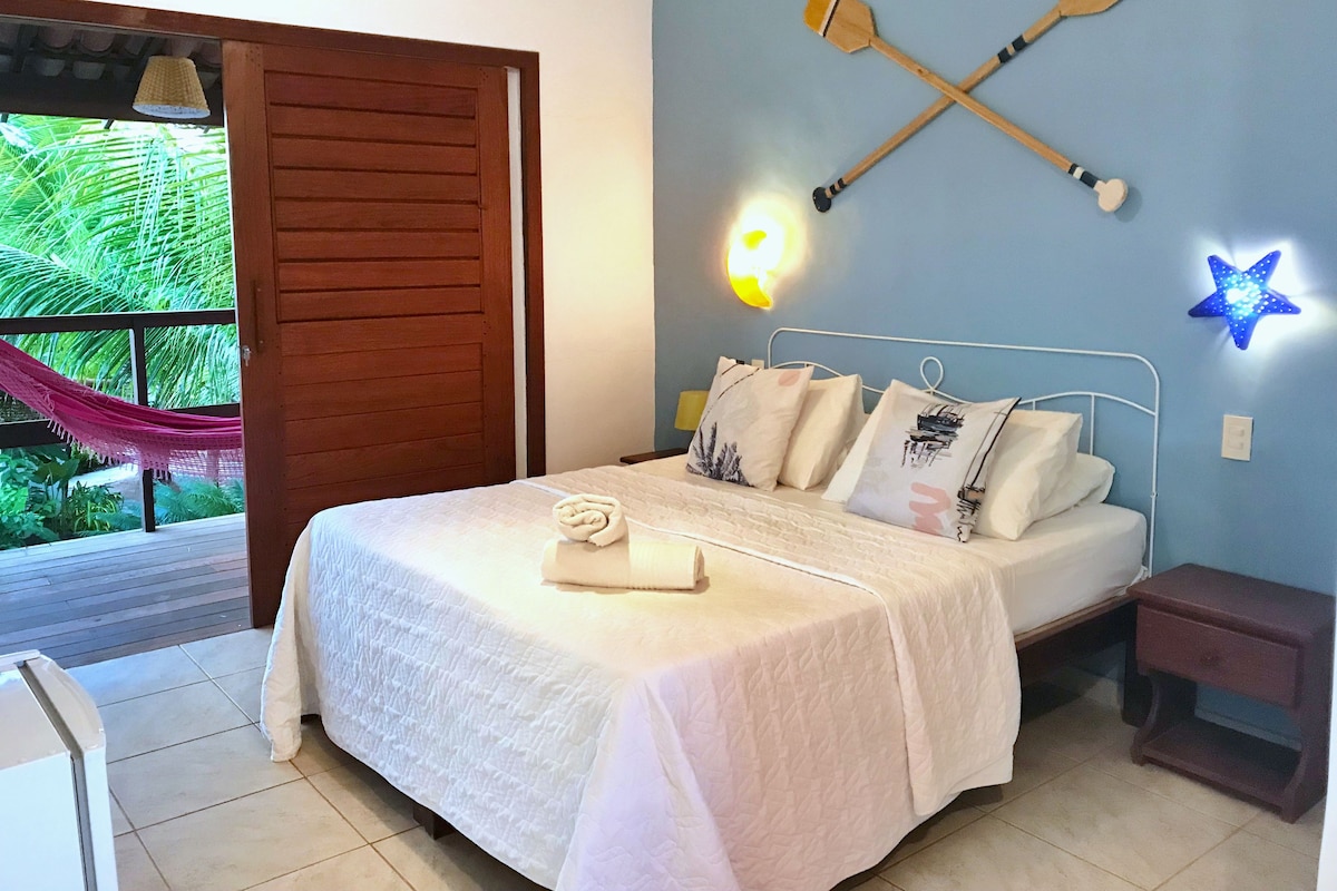 Une chambre à coucher avec un lit, une porte en bois, un hamac et des lampes fixées au mur.